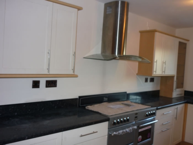 Cream units with a black worktop, range cooker and stainless chimney hood