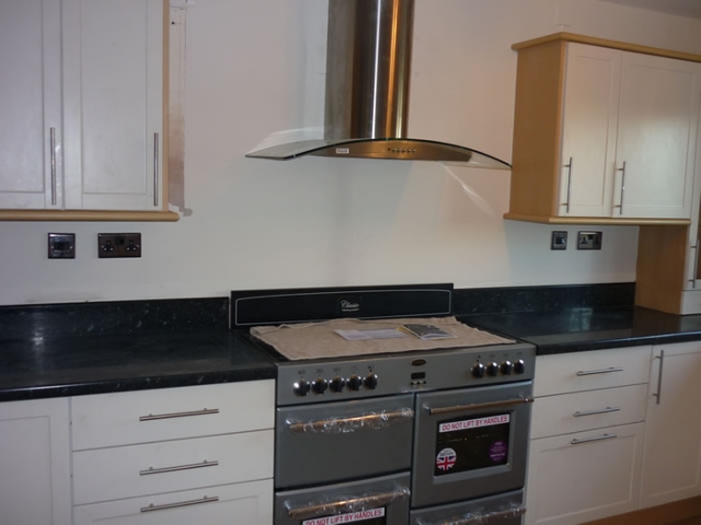 Cream units with a black worktop and a range cooker under a stainless chimney hood